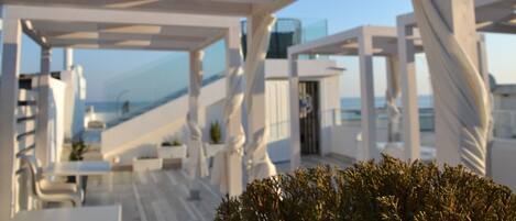 An outdoor terrace with white structural elements and a view of the sea.