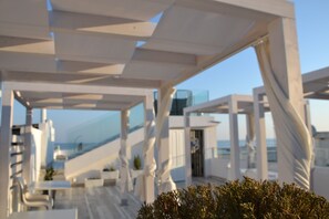 An outdoor terrace with white structural elements and a view of the sea. - Quintessenza - Charme Rooms (Vieste)
