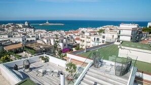 A rooftop terrace with a view of the sea, white buildings, and a lighthouse in the distance. - Quintessenza - Charme Rooms (Vieste)
