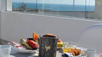 A balcony with a table set for breakfast, including croissants, fruit, and a coffee pot.