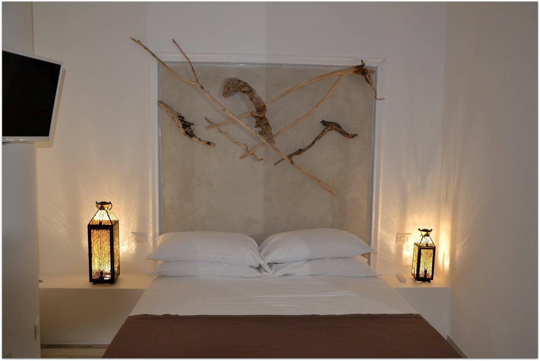 A bedroom with a bed, two bedside tables, two wall-mounted lamps, and a mounted TV.