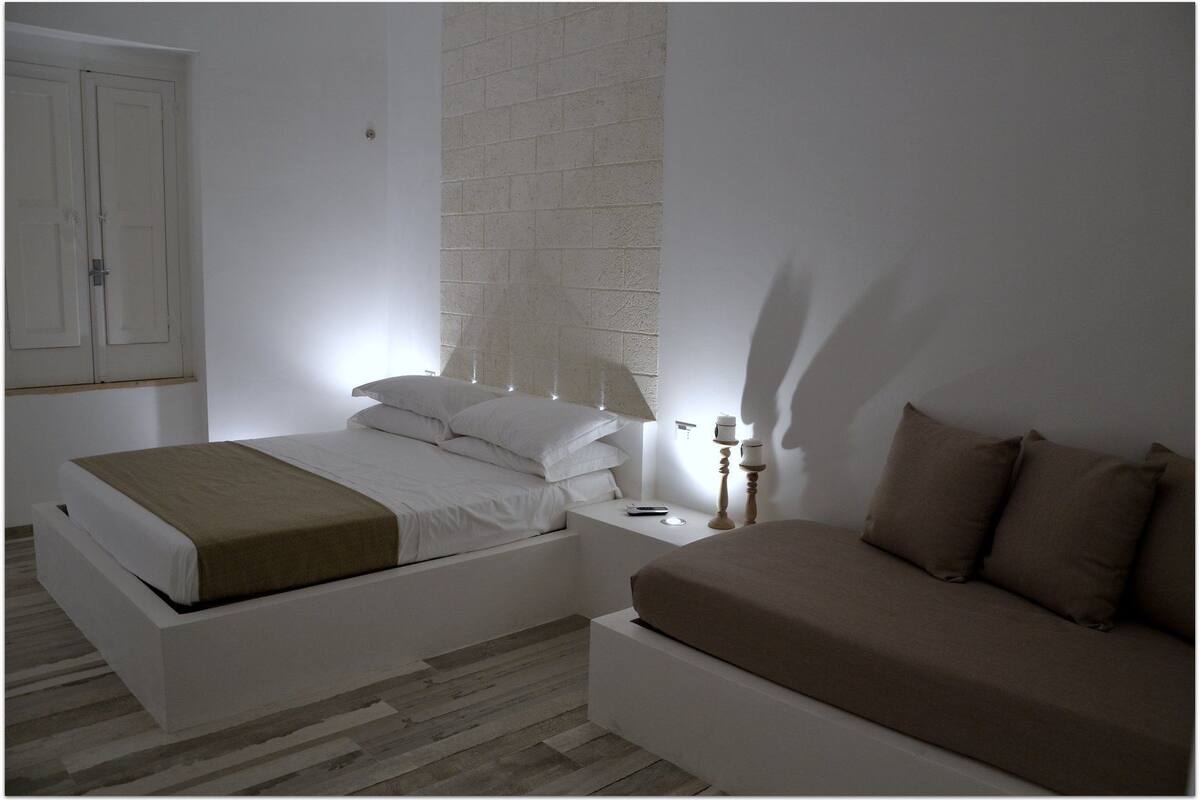 Une chambre à coucher au style minimaliste, comprenant un lit, une table de chevet, une lampe et une petite table d’appoint.