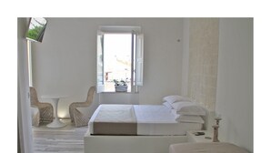 A bedroom with a bed, two chairs, a small table, and a window with a view of the outside. - Quintessenza - Charme Rooms (Vieste)