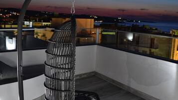 Een hangstoel op een balkon met uitzicht op de skyline van de stad in de schemering.