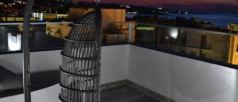 Una silla colgante en un balcón con vista al horizonte urbano al anochecer.