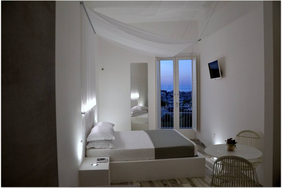 Une chambre à coucher comprenant un lit, une table de chevet, une chaise et une petite table sur laquelle est posée une plante.