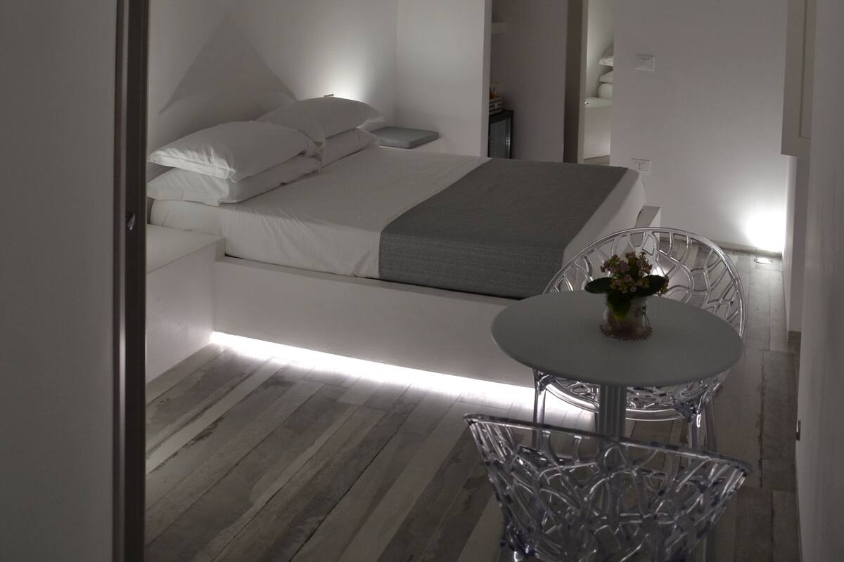 Une chambre à coucher moderne avec un lit, une table de chevet et une petite table ronde sur laquelle est posé un vase.