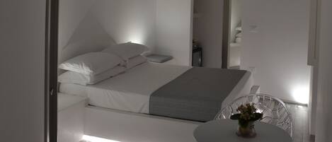 Un dormitorio moderno con cama, mesita de noche y una pequeña mesa redonda con un florero.