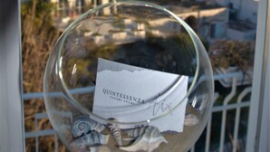 A glass with a label reading "QUINTESSENZA CHARME ROOMS" and a view of a coastal town through the glass. - Quintessenza - Charme Rooms (Vieste)
