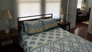 Un dormitorio con una cama, dos mesitas de noche, una lámpara y una silla en la habitación contigua.