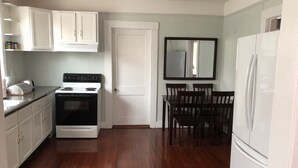 Una cocina compacta con gabinetes blancos, estufa, refrigerador y una mesa de comedor con sillas.