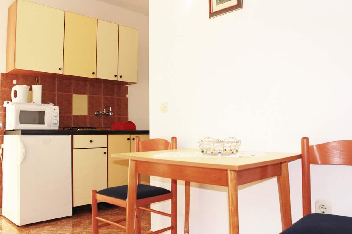A compact kitchen with a microwave, a small refrigerator, and a dining table with chairs.