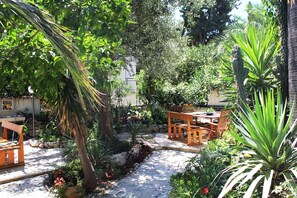 A patio area with a stone pathway, wooden furniture, and various plants. - Antonio Apartments Orebic (Orebic)
