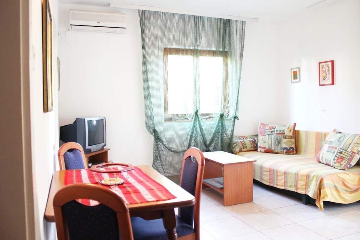 A room with a dining table, chairs, a television, a sofa, and a window with curtains.