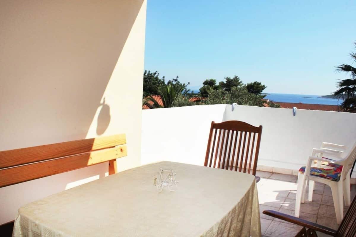 A balcony with a table and chairs, overlooking a coastal view with vegetation and a clear sky.