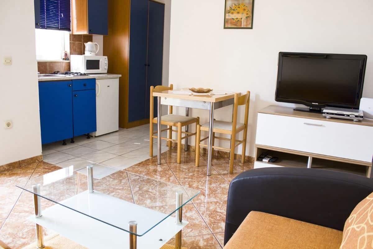 A compact living space with a kitchenette, a dining area, a flat-screen TV, and a glass-top coffee table.
