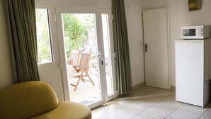 Ein Zimmer mit einer Couch, einer Mikrowelle, einer Schiebetür zu einem Außenbereich mit Stuhl und Tisch sowie einer weiteren Tür.