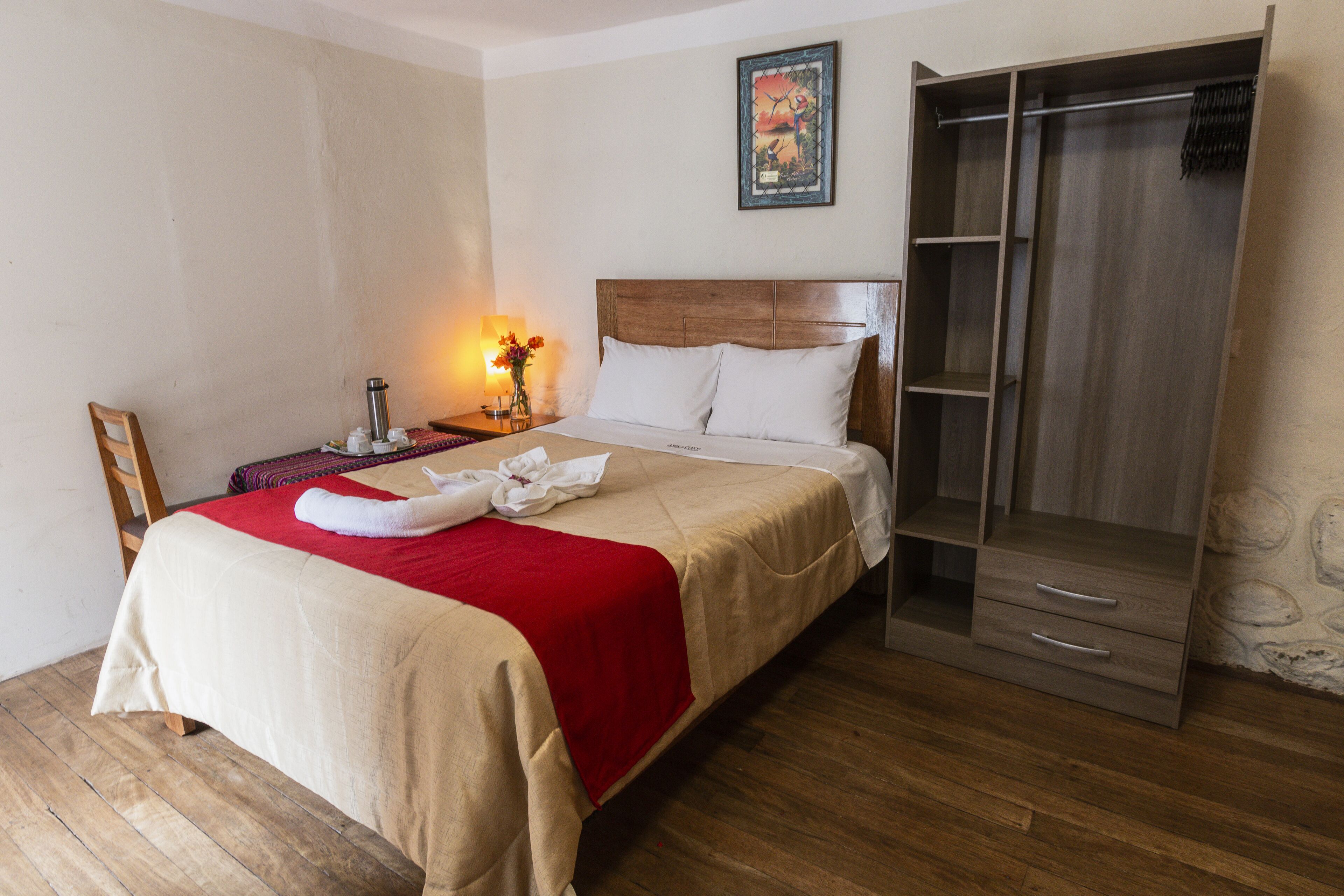 A hotel room with a bed, a nightstand, a lamp, a wardrobe, and a painting on the wall.