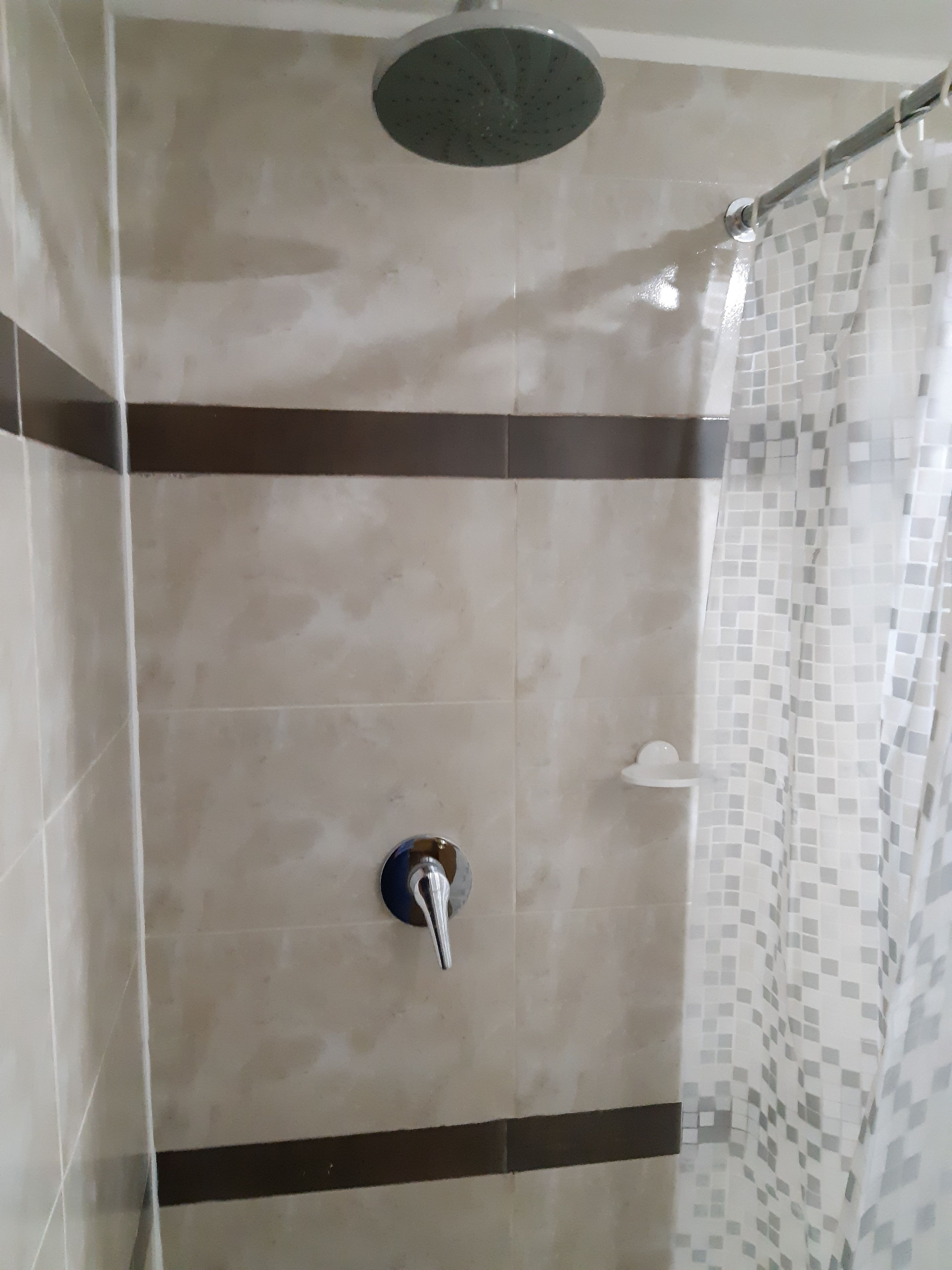 Ducha con cabezal de ducha tipo lluvia, cabezal de ducha de mano y pared de azulejos con diseño de cuadros.