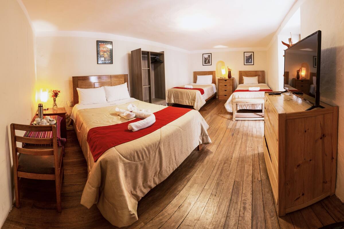Ein Hotelzimmer mit zwei Betten, Holzboden, Fernseher und einem Kleiderschrank.