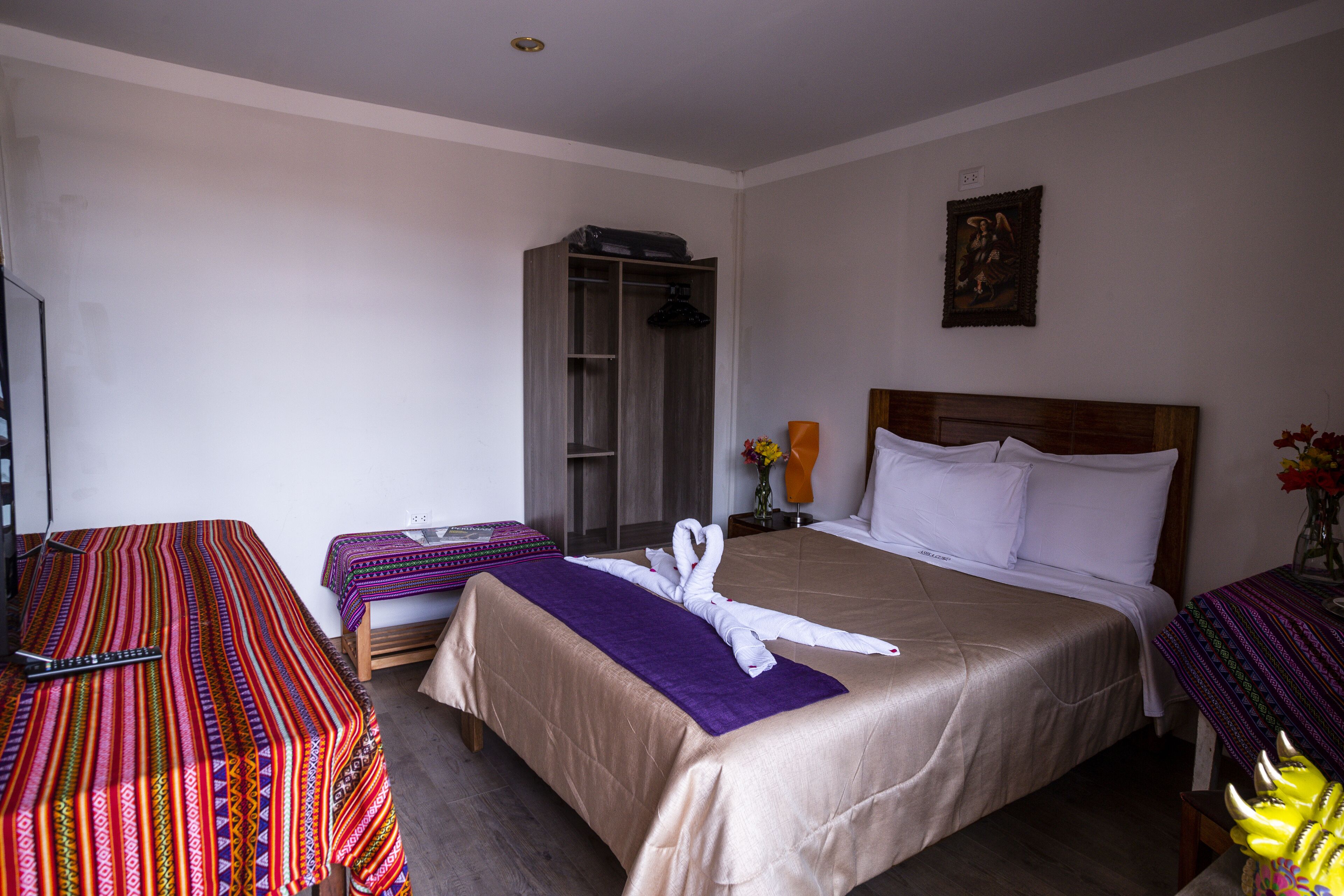 A hotel room with a large bed, a wardrobe, a bedside table with a lamp, and a small table with flowers.