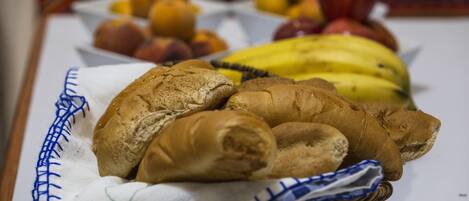 A table with a basket containing croissants and a plate with fruits.