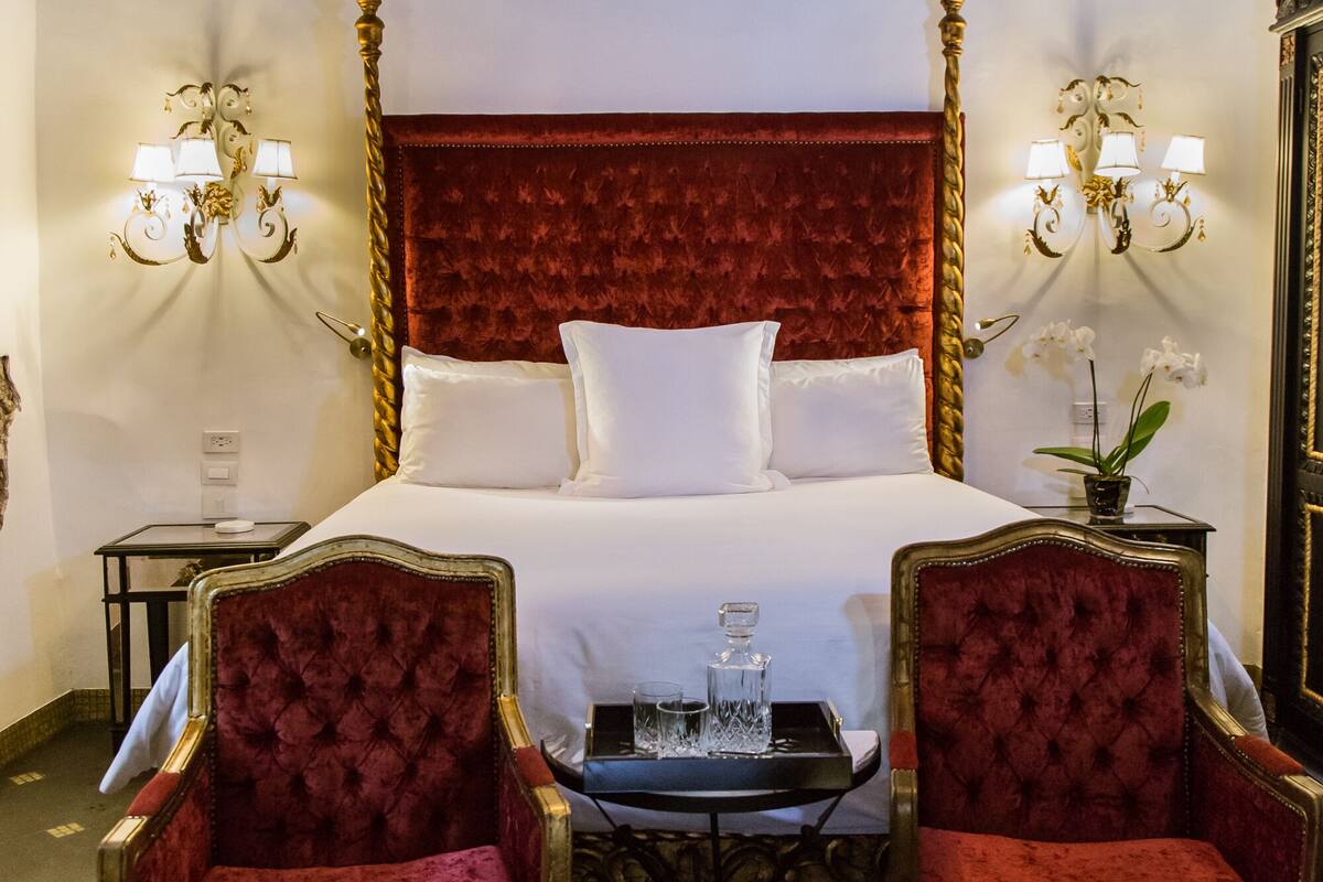 Une chambre à coucher luxueuse, dotée d’un grand lit, d’un lustre somptueux et de deux fauteuils rouges à revêtement en tissu.