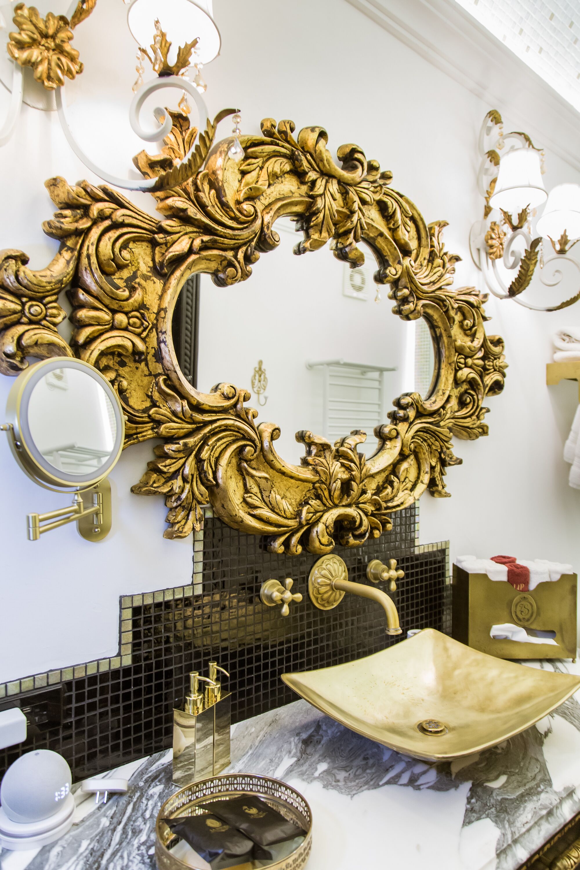 A bathroom with a large ornate gold mirror, a marble sink, and a black tiled backsplash.
