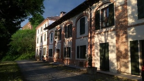 A row of traditional buildings with arched windows and brick facades, a paved driveway, and a tree-lined street. - La Cascina del Castello (Asti)