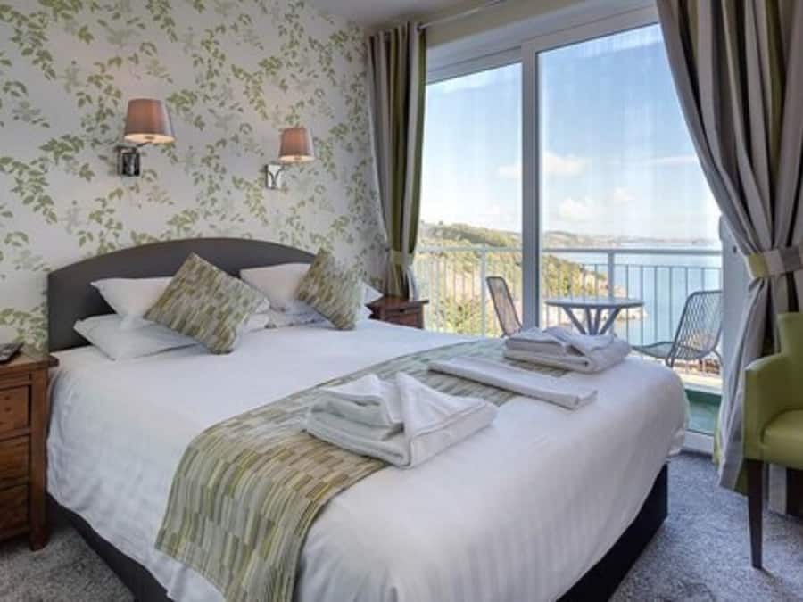 Une chambre d’hôtel avec un grand lit, une table de chevet, une chaise et un balcon avec vue.