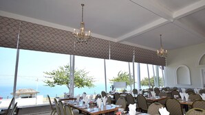 A restaurant with tables set for dining, large windows offering a view of the sea, and chandeliers hanging from the ceiling. - The Babbacombe Hotel (Torquay)