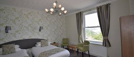 A bedroom with two beds, a chandelier, a window with curtains, and a radiator.