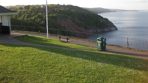 A grassy area with a bench and a trash bin near a coastal path. - The Babbacombe Hotel (Torquay)
