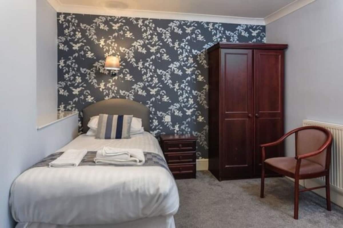 Um quarto com cama, mesa de cabeceira, guarda-roupa e uma cadeira.
