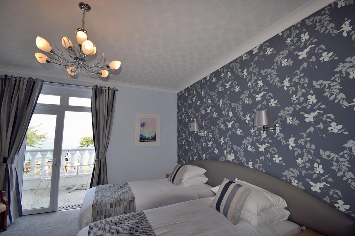Quarto de hotel com uma cama grande, um candelabro, uma varanda com cadeiras e papel de parede floral.
