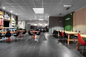 Un restaurante moderno con varias mesas y sillas, una estantería con libros, y una pared verde con líneas verticales.