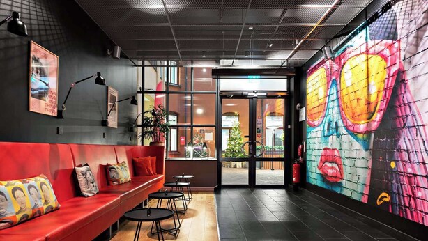 A modern interior with a red sofa, black round tables, and a colorful mural on the wall. - Connect hotel city (Stockholm)