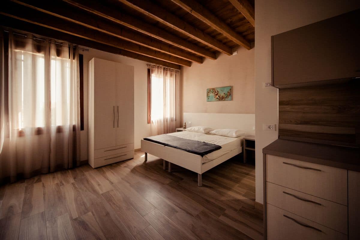 A bedroom with a wooden ceiling, a bed, a wardrobe, and a painting on the wall.