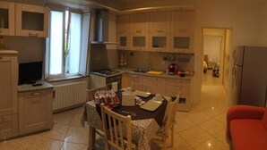 Een kleine keuken met een eettafel, een koelkast en een bank in een woongedeelte.