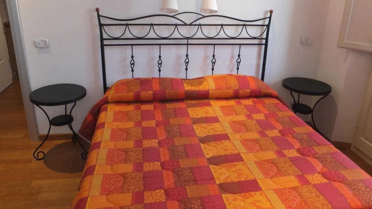 Ein Bett mit einem gemusterten Überwurf, einem Metall-Kopfstück und zwei kleinen Nachttischen.