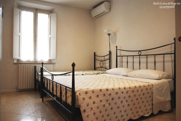Un dormitorio con una cama individual, un radiador, una ventana con contraventanas y un equipo de aire acondicionado.