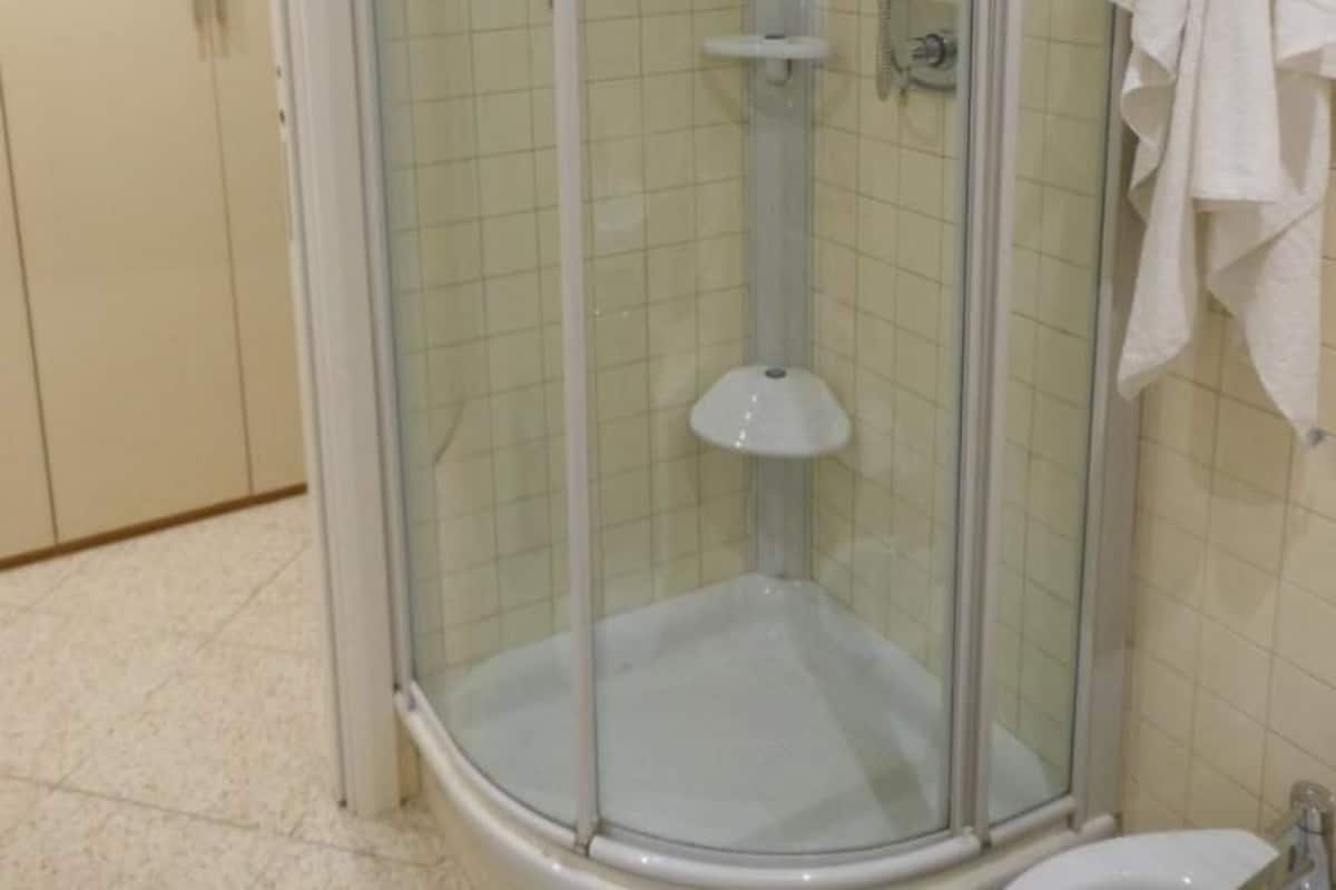 Una ducha en esquina con puerta de cristal, un lavabo blanco y una toalla colgada en la pared.