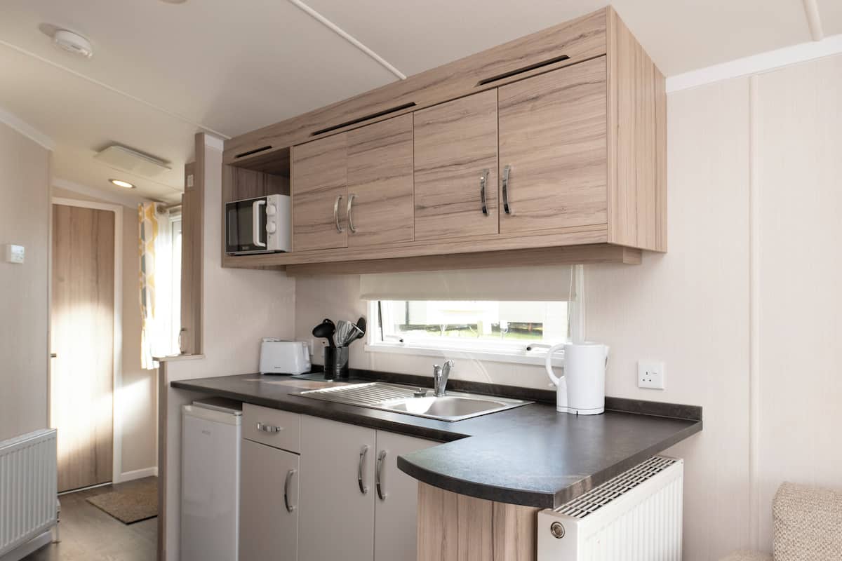 A compact kitchen with a microwave, sink, and dishwasher, wooden cabinets, and a window providing natural light.