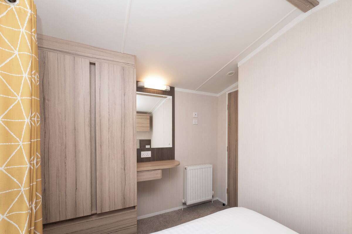 A bedroom with a wardrobe, a bedside table, a radiator, and a mirror.