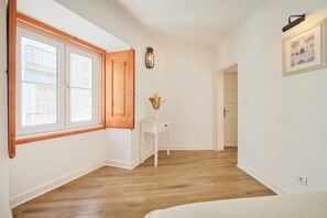 A room with wooden flooring, a white wall, a door, a small white table with a vase, and a framed picture. - Casa do Mercado Lisboa (Lisbon)
