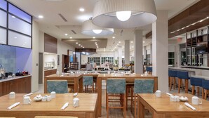 Un comedor moderno con mesas y sillas de madera, vajilla blanca y un candelabro central.