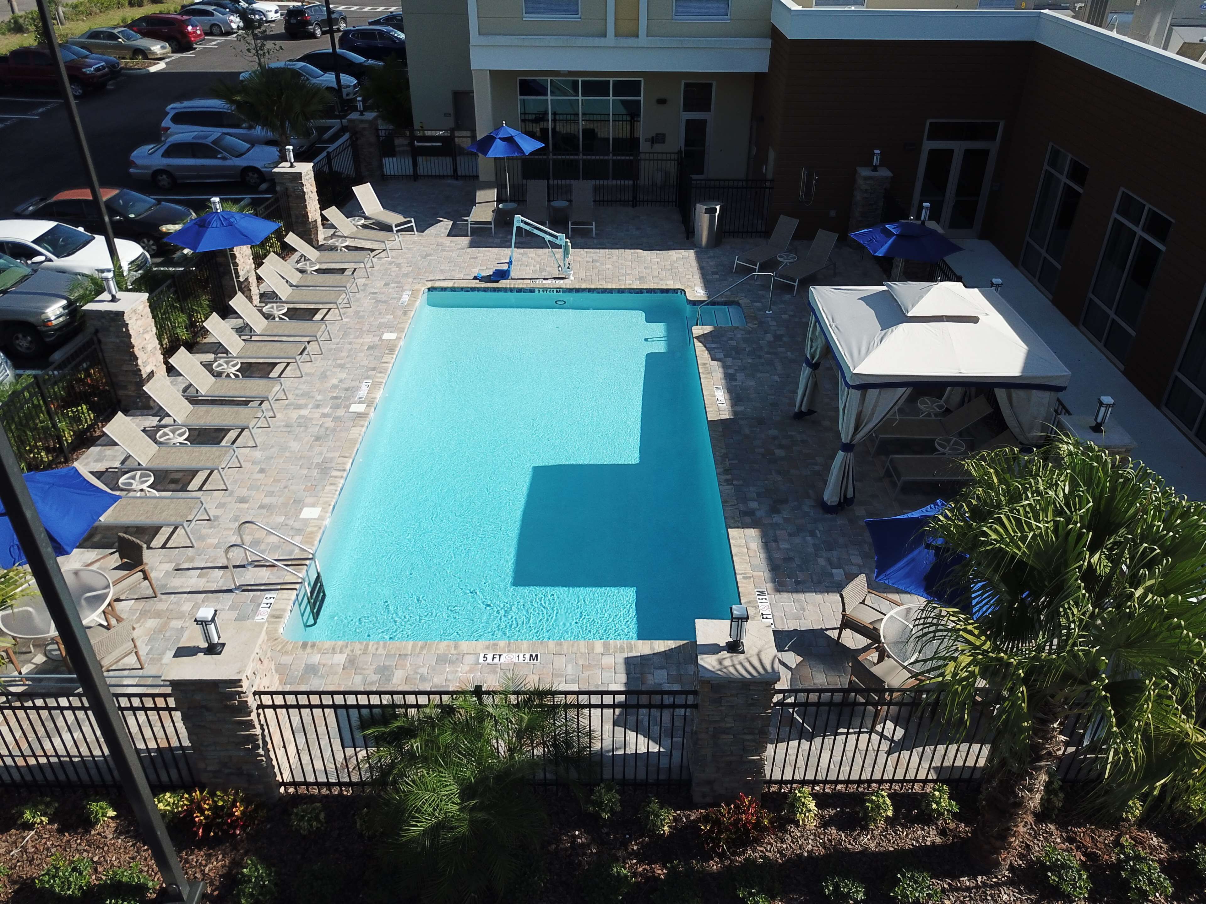 A swimming pool with lounge chairs and umbrellas, surrounded by a parking area and a building.