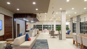 Un hall d’entrée spacieux, avec un canapé, des fauteuils, une table à manger et une grande fenêtre.