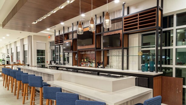 Zona de bar moderna con una barra alargada, varios taburetes y una amplia variedad de botellas y vasos.