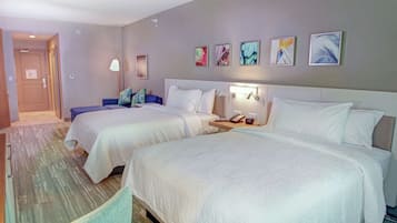 Habitación de hotel con dos camas, una mesita de noche con lámpara y una obra de arte en la pared.
